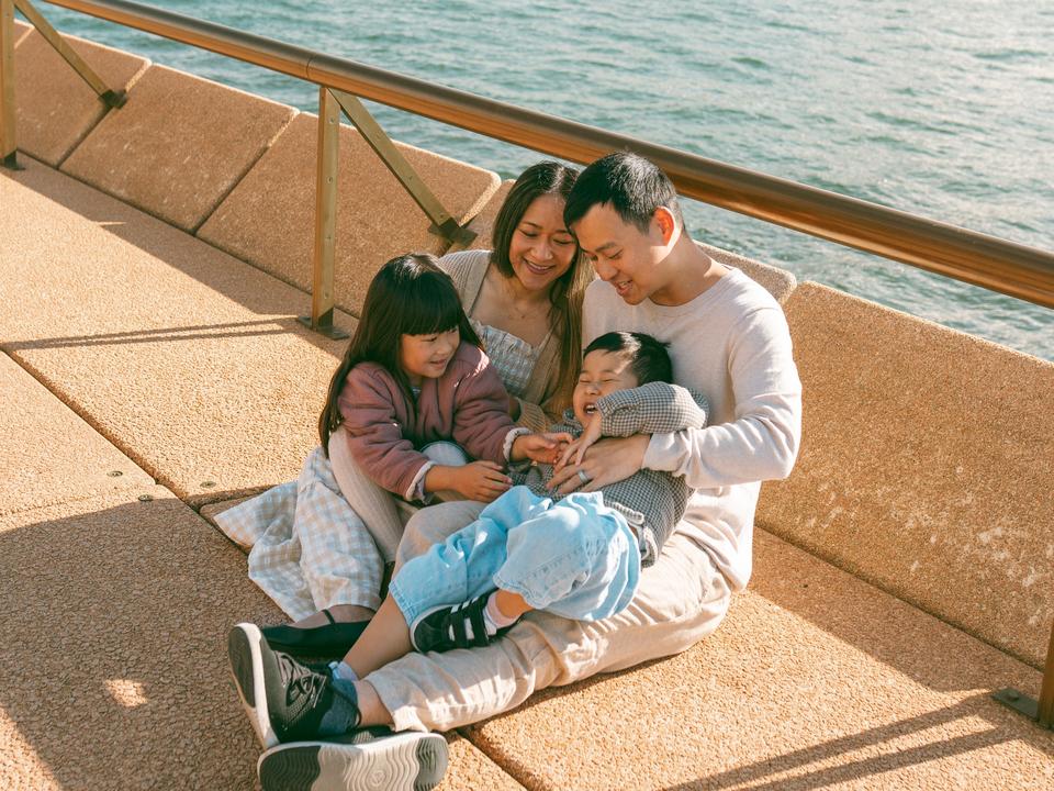 Michael, Alice, Ruby and Rylo sitting together on a harbour promenade, laughing, with the water behind them